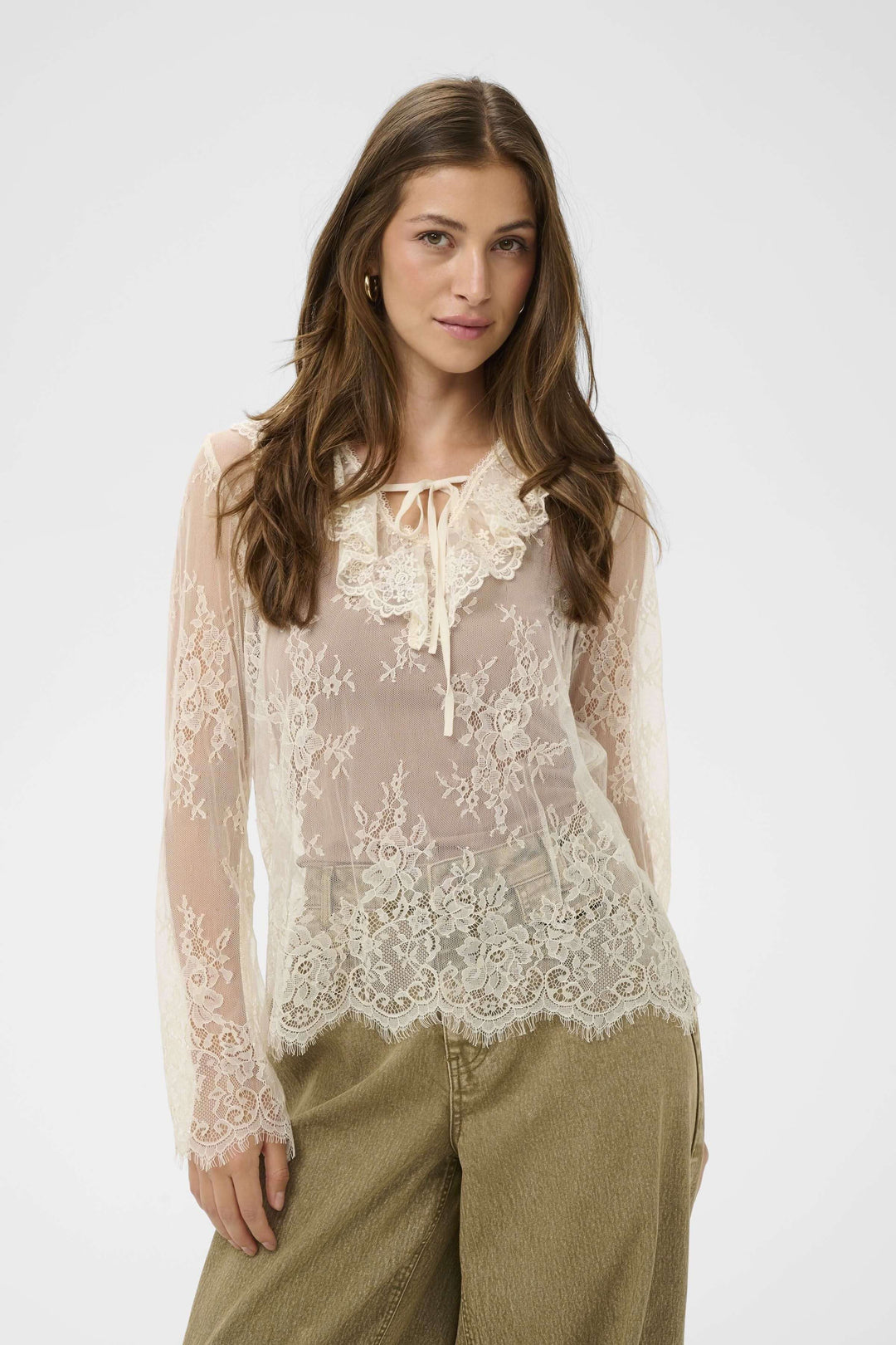 Blouse Mira en dentelle transparente à manches longues, silhouette romantique avec col orné et lien à nouer, tenue élégante.