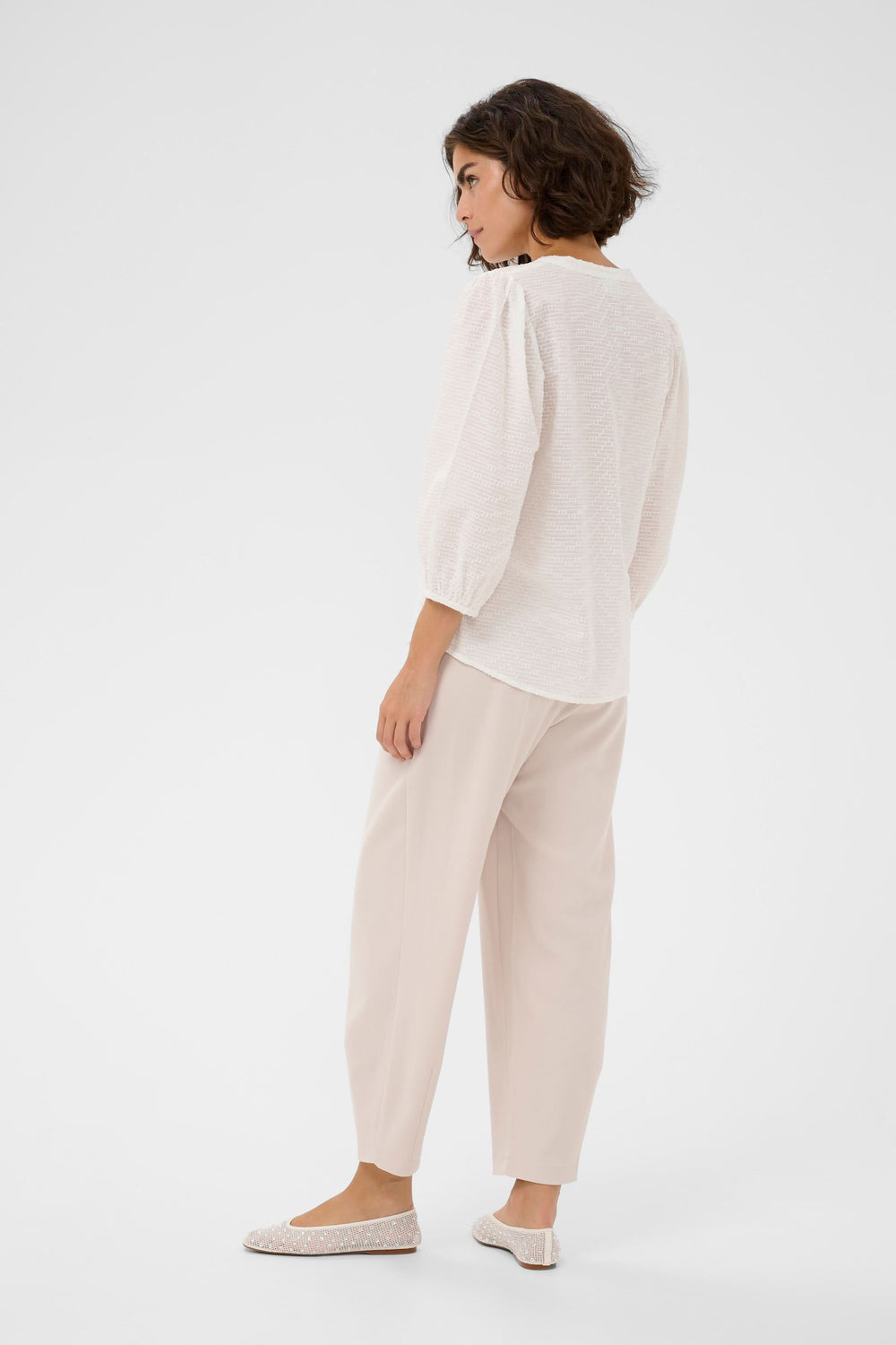 Femme portant la Blouse Penelope texturée à manches trois-quarts, encolure en V, tissu léger et confortable.