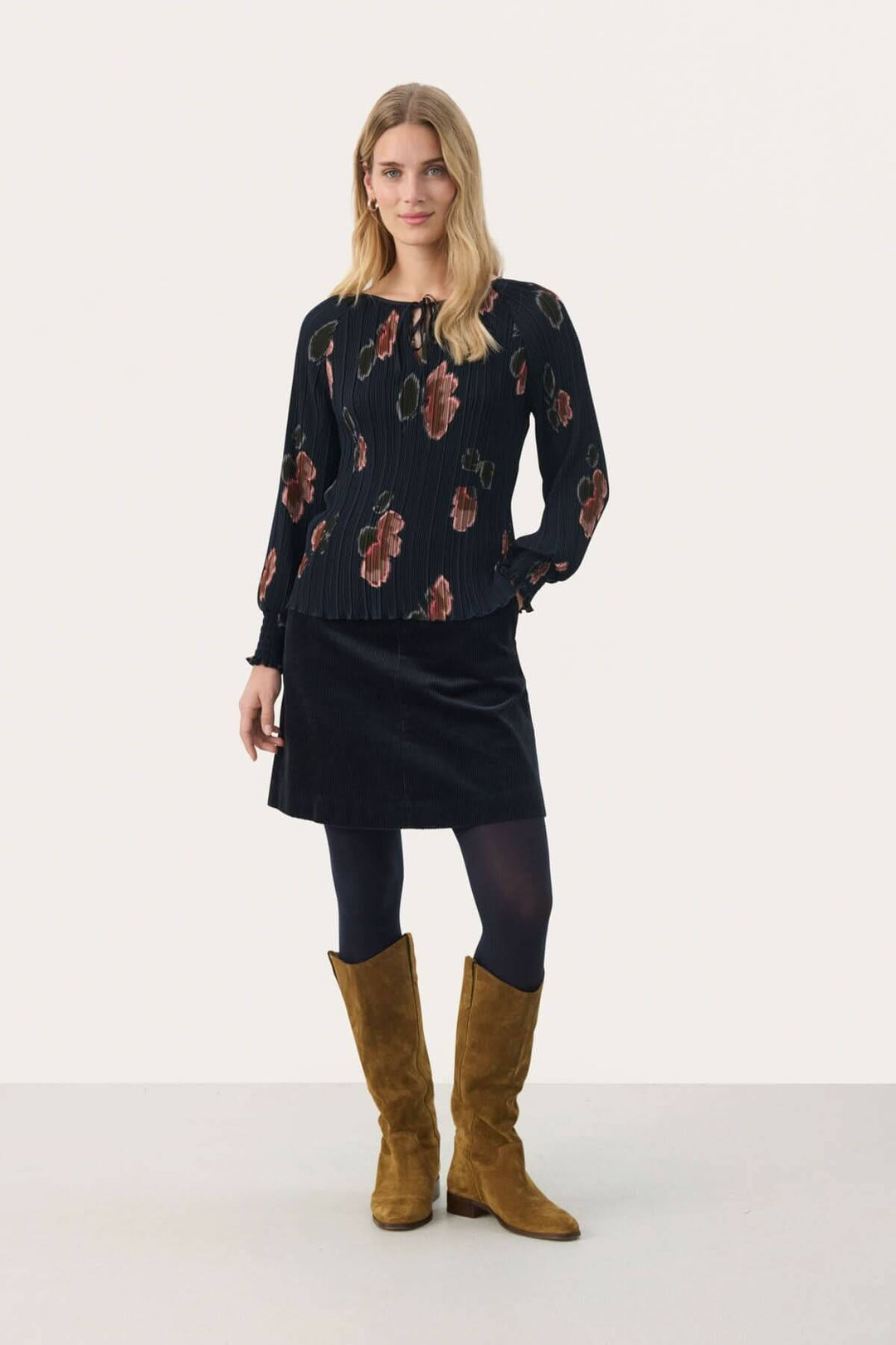 Blouse Priya femme élégante à imprimé floral, manches longues et encolure à nouer, portée avec une jupe.