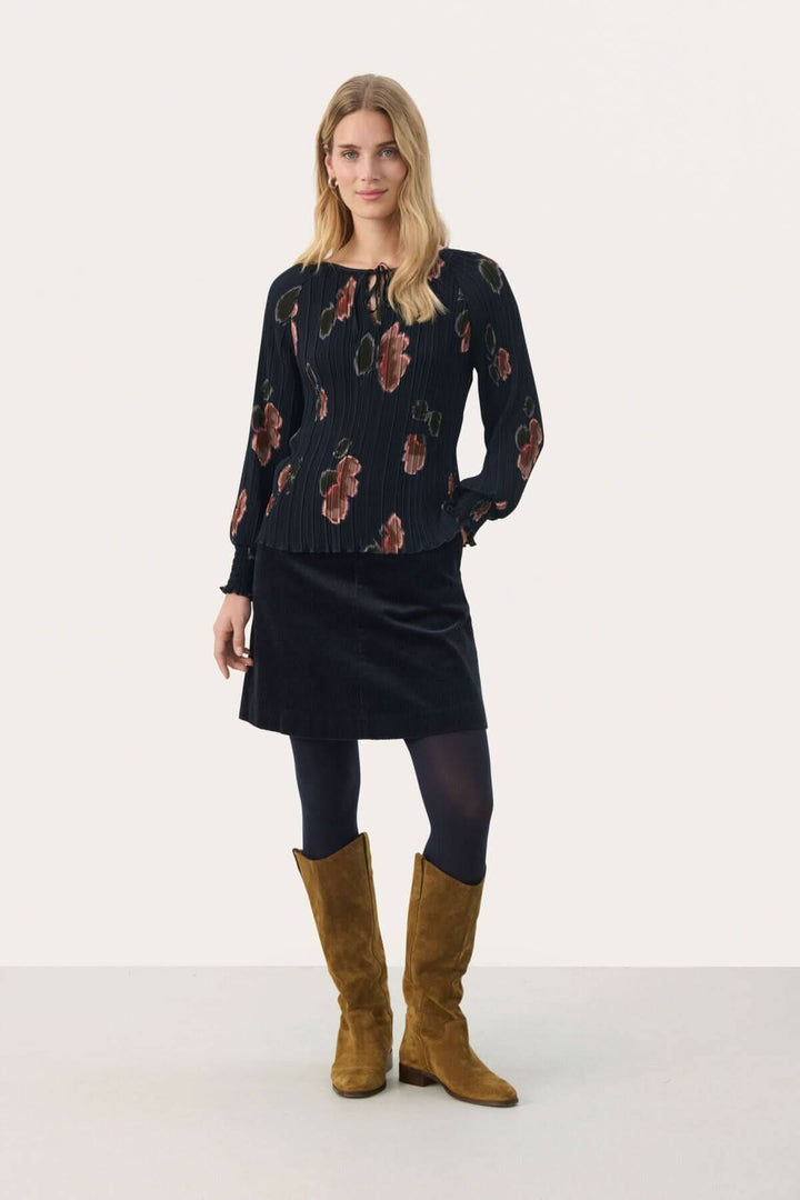 Blouse Priya femme élégante à imprimé floral, manches longues et encolure à nouer, portée avec une jupe.