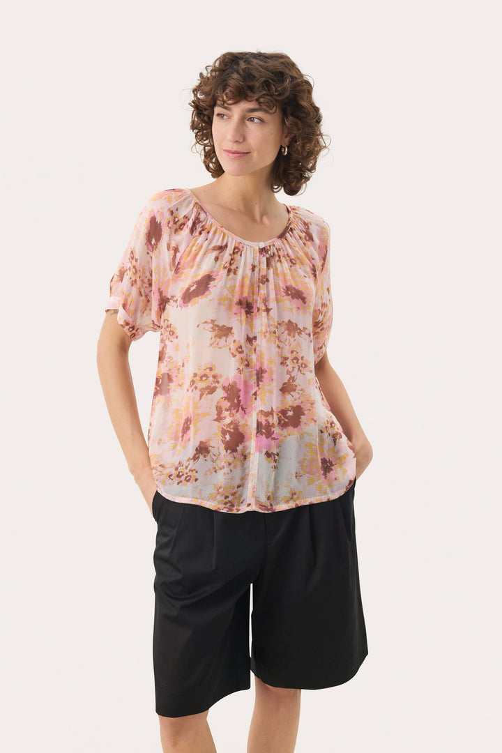 Blouse légère rosanne à imprimé floral, avec encolure froncée et manches courtes, portée avec un short.