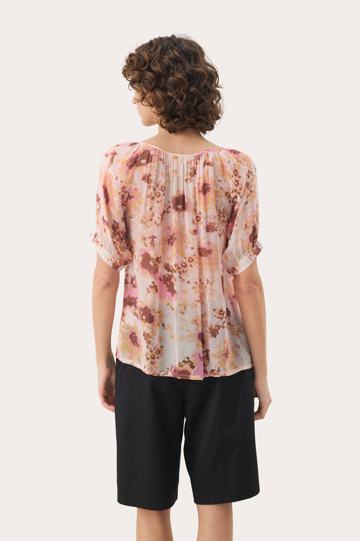 Femme portant une blouse Rosanne à imprimé floral, vue arrière, avec des manches courtes et une coupe fluide.