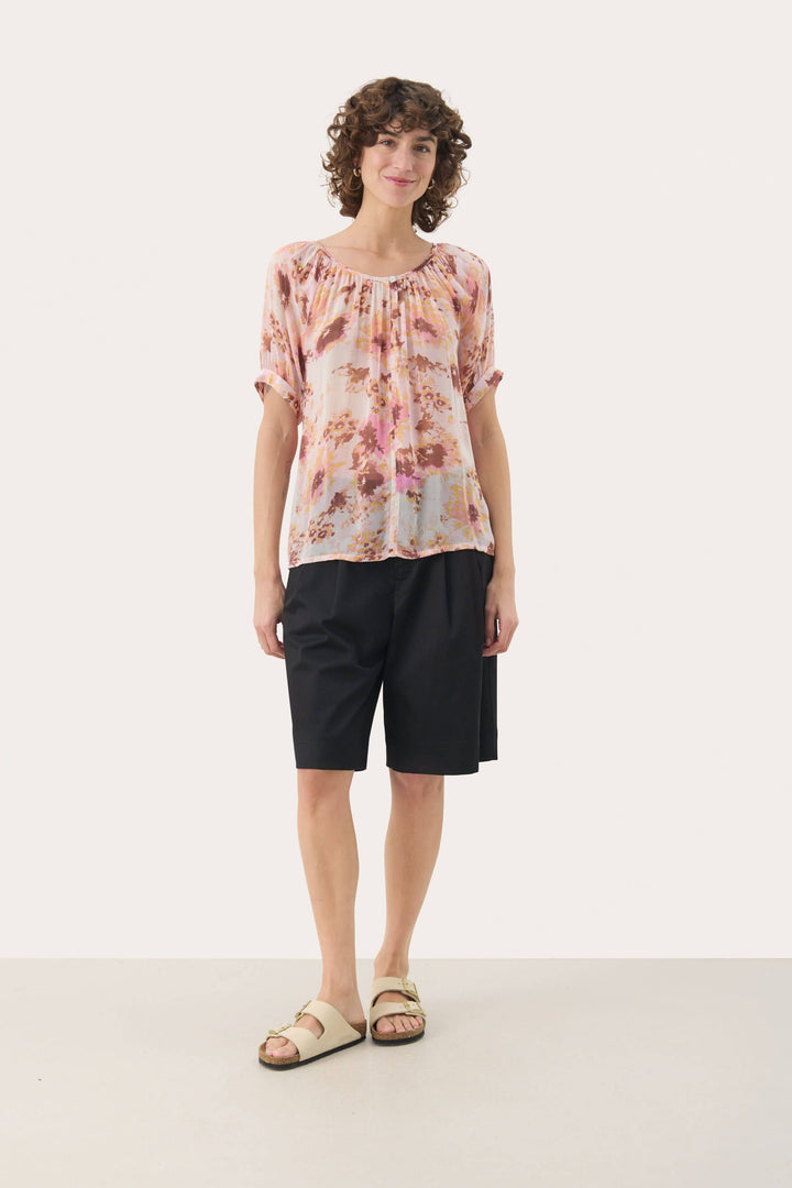Blouse Rosanne légère à imprimé floral, manches courtes, portée avec un short noir, style décontracté et féminin.