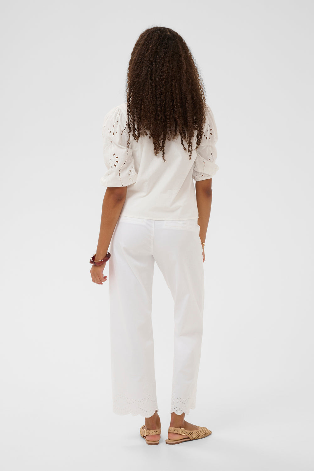 Vue arrière de la Blouse Signe avec détails ajourés et manches bouffantes, portée avec un pantalon blanc, style élégant et décontracté.