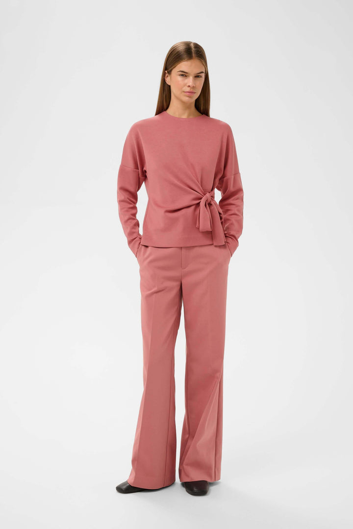 Femme portant une Blouse Tricent rose avec détail noué, coupe flatteuse et design contemporain.