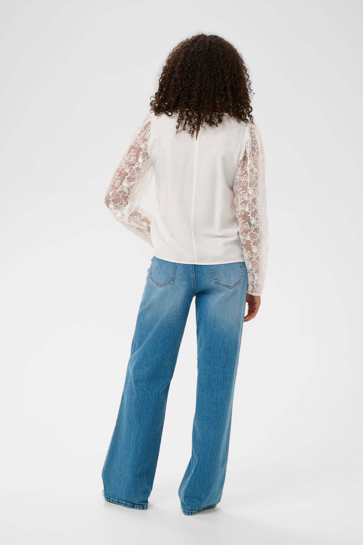 Blouse avec broderie sur mannequin vue arrière, manches longues en dentelle et coupe droite, associée à un jean pour un look quotidien.