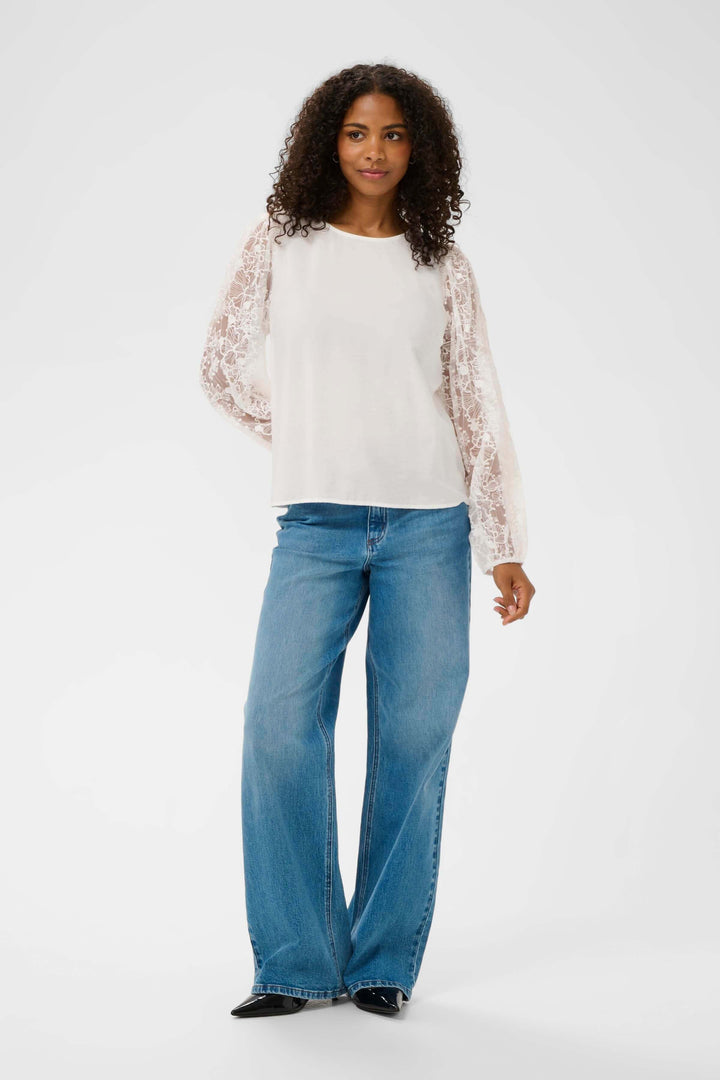 Blouse avec broderie élégante avec manches longues en dentelle, portée par un mannequin avec jean pour un look décontracté.