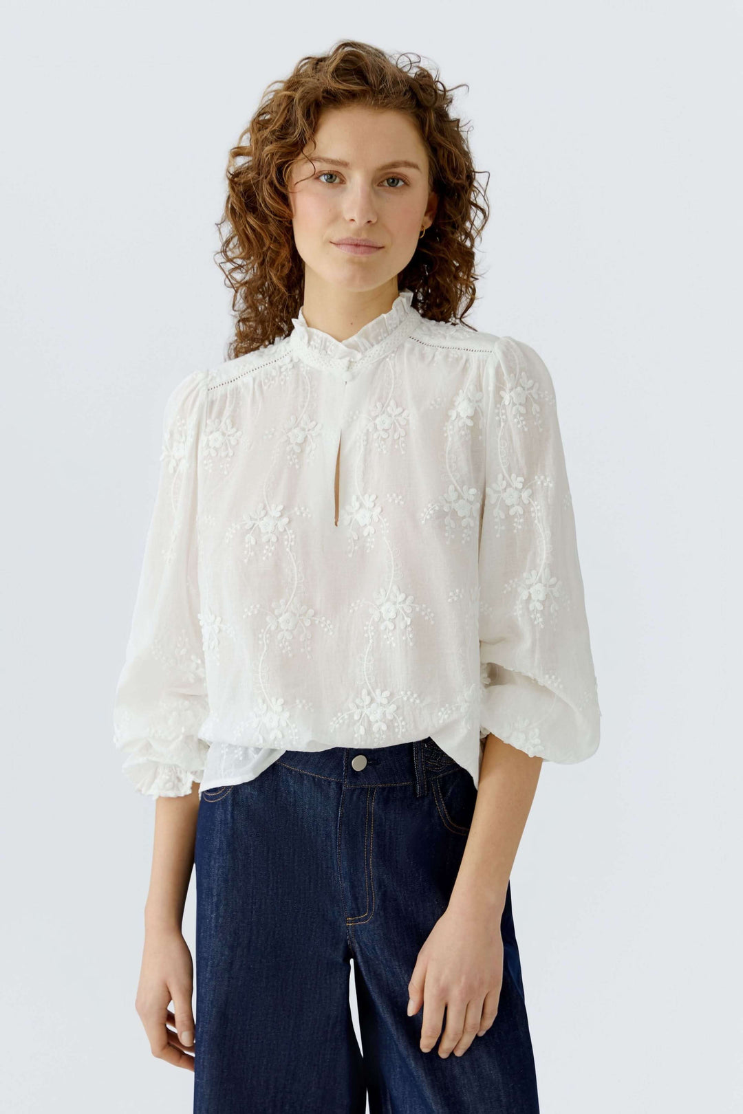 Blouse à broderies florales blanche avec col montant et manches longues, portée par un modèle.