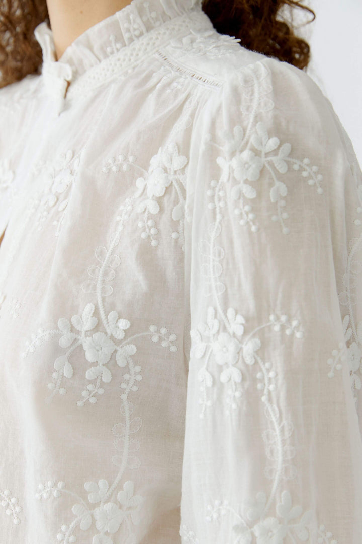 Blouse à broderies florales délicate avec col montant élégant et motif floral raffiné, parfaite pour une tenue féminine et élégante.