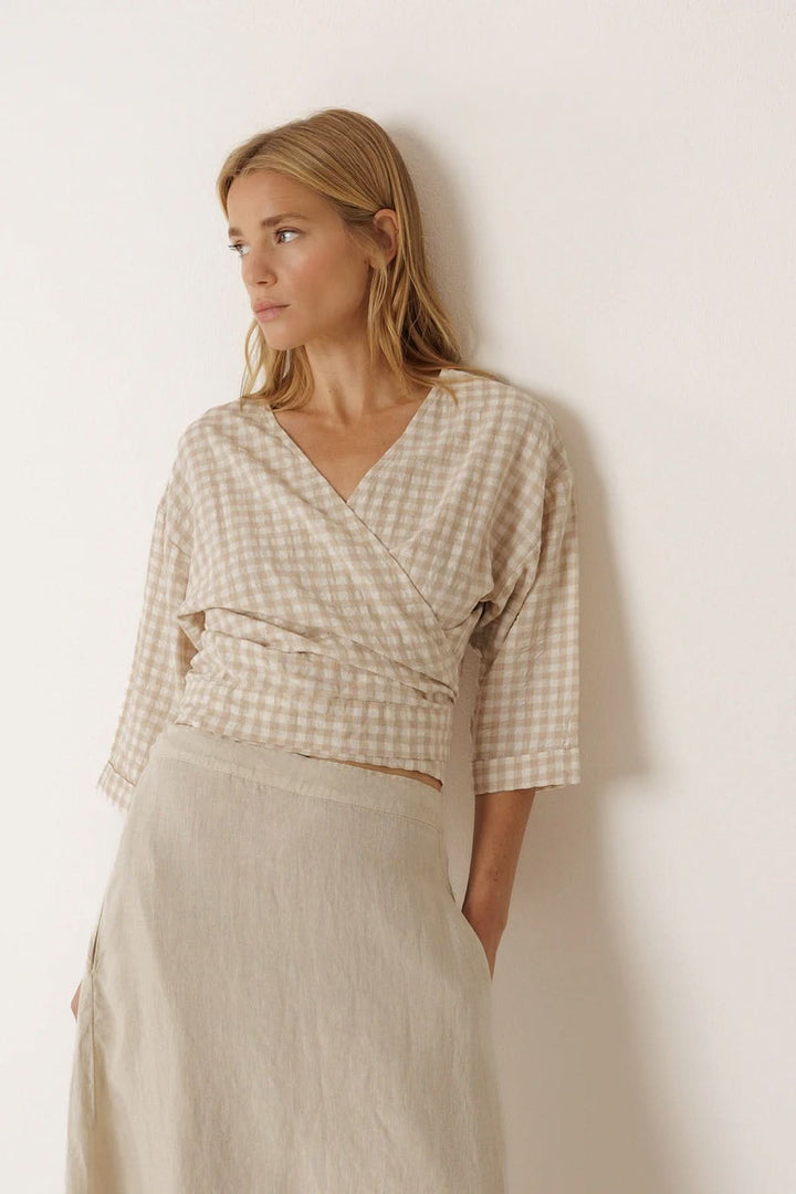 Femme portant une blouse cache-cœur à motif vichy avec manches 3/4 et encolure en V croisée dans une tenue élégante et moderne.