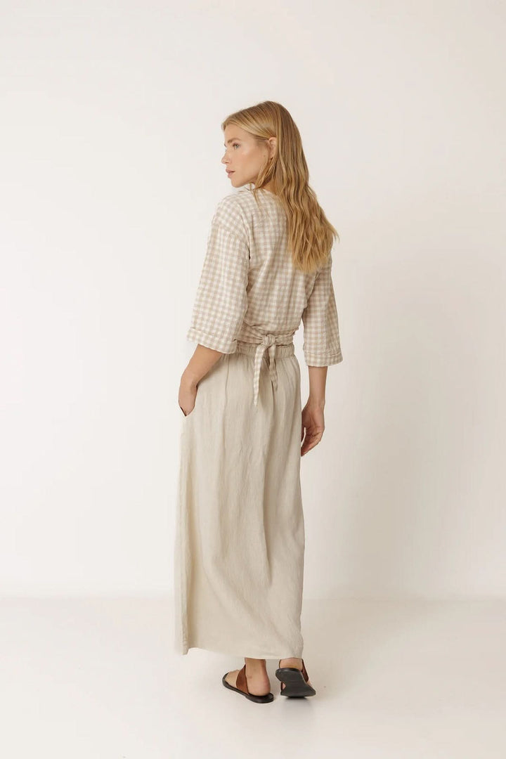 Femme portant une blouse cache-cœur à motif vichy avec manches 3/4 et jupe longue, vue de dos, style féminin et contemporain.