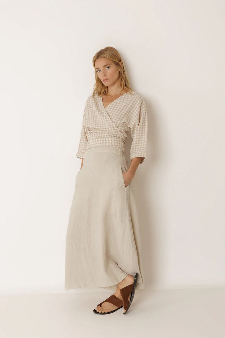 Femme portant une blouse cache-cœur à motif vichy avec manches 3/4, associée à une jupe longue fluide, style féminin et contemporain.