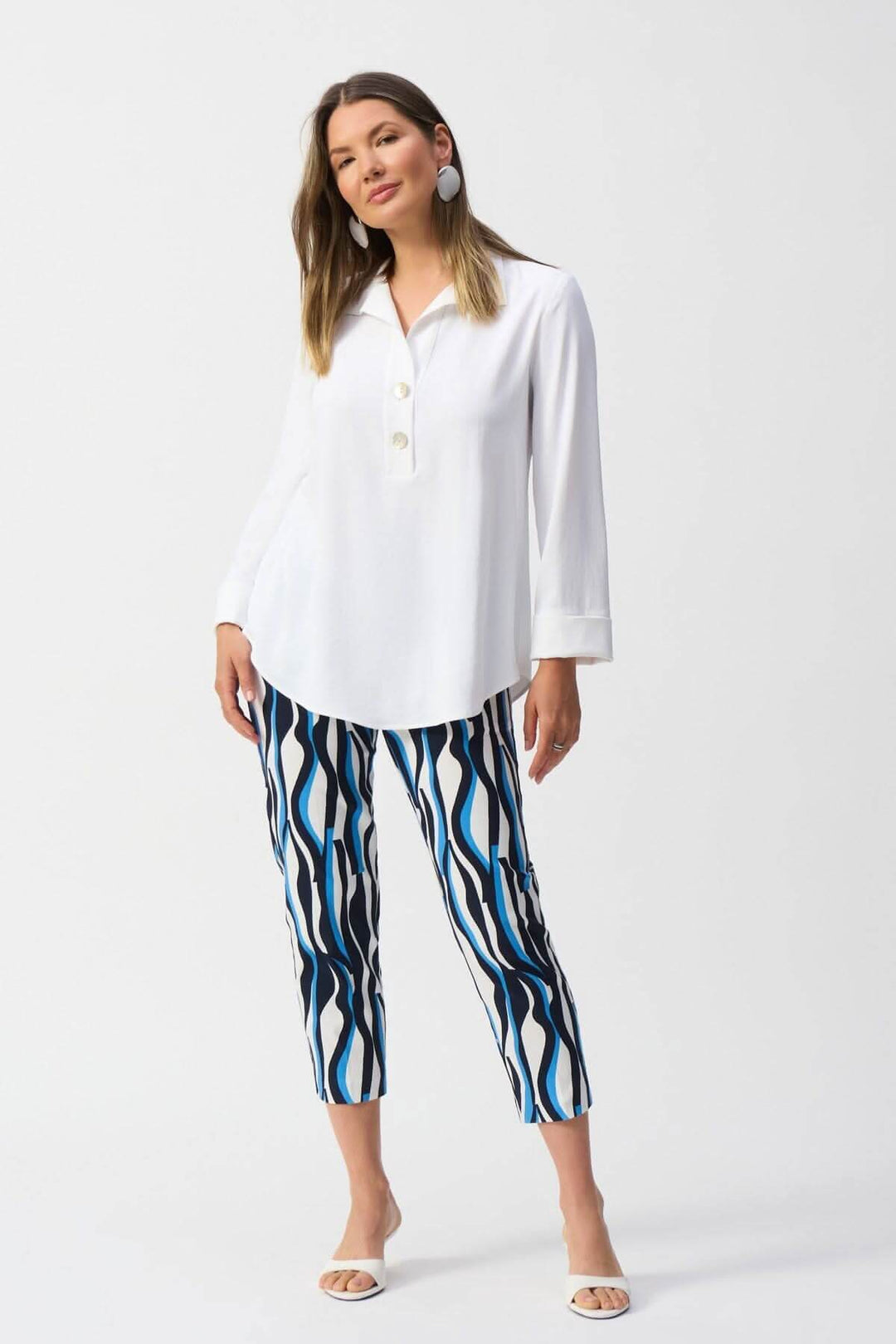 Femme portant une blouse classique blanche avec un col en V et un pantalon à motifs ondulés, style élégant.