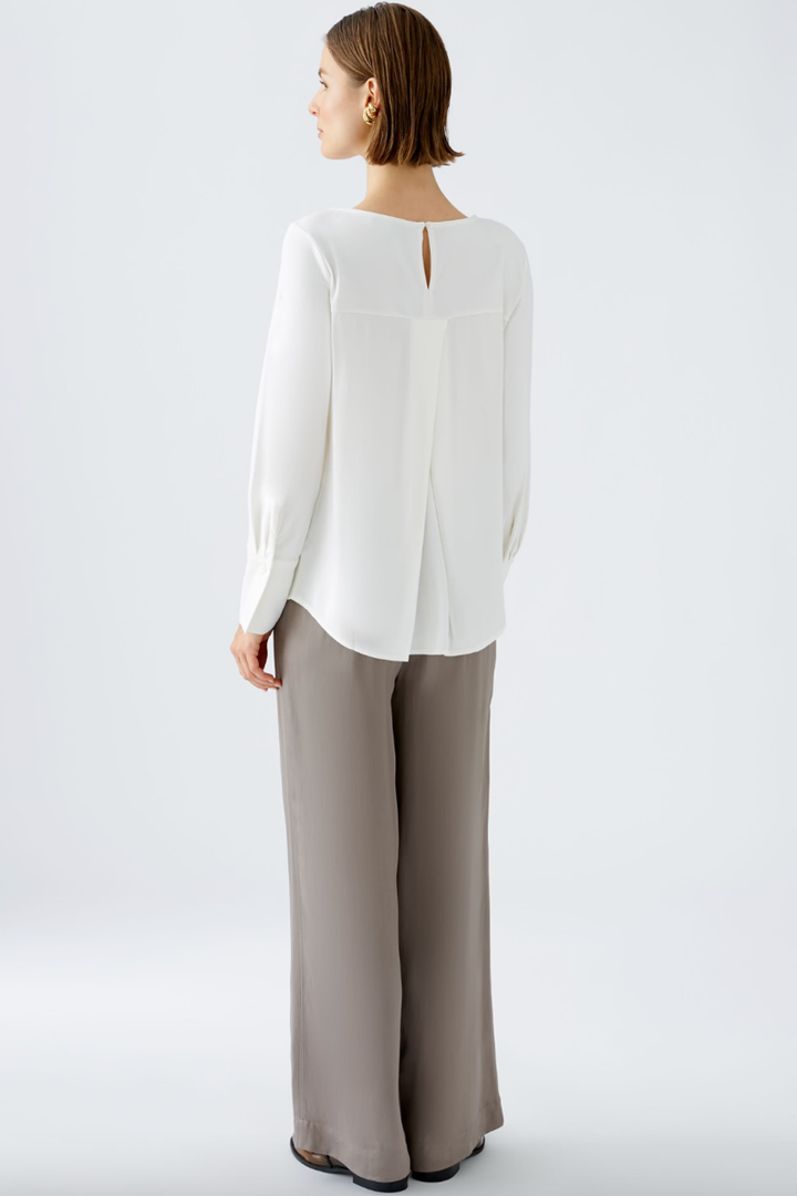 Chemise décontractée blanche avec un col rond et une fente au dos, portée avec un pantalon ample.