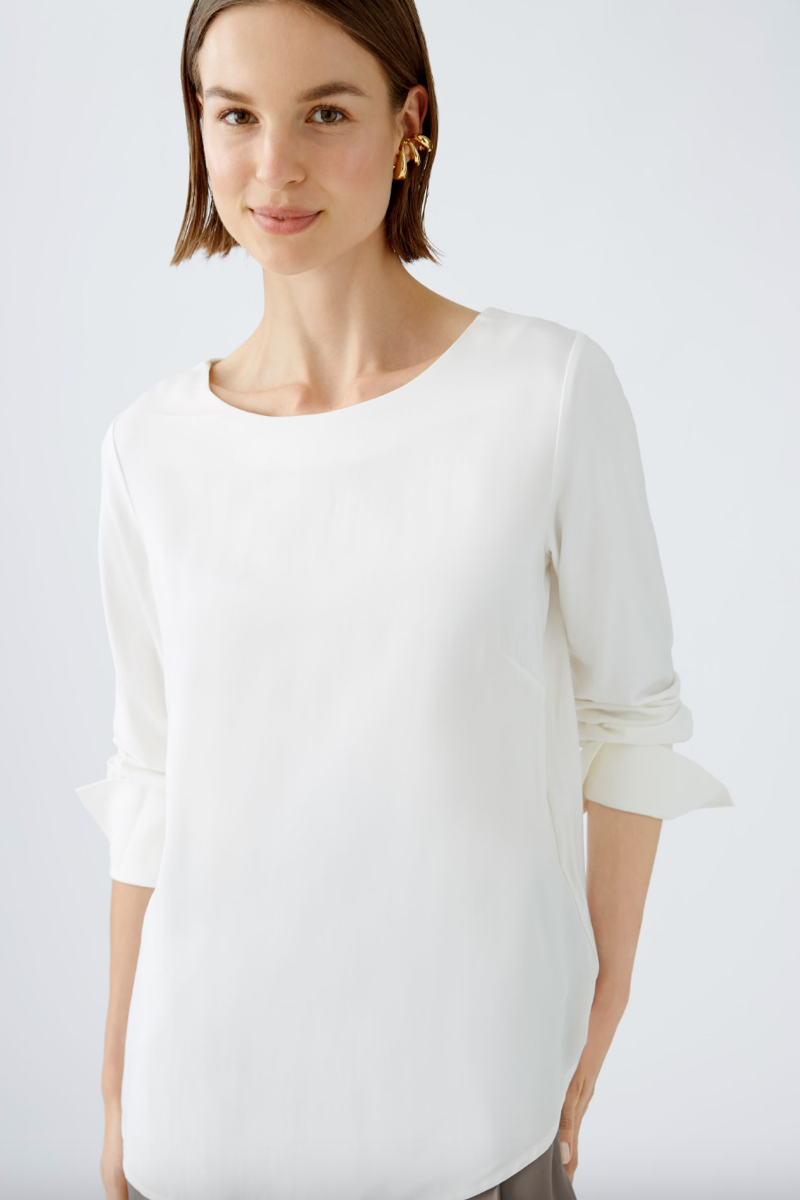 Blouse décontractée en satin blanc avec col rond et manches longues, alliant confort et élégance.