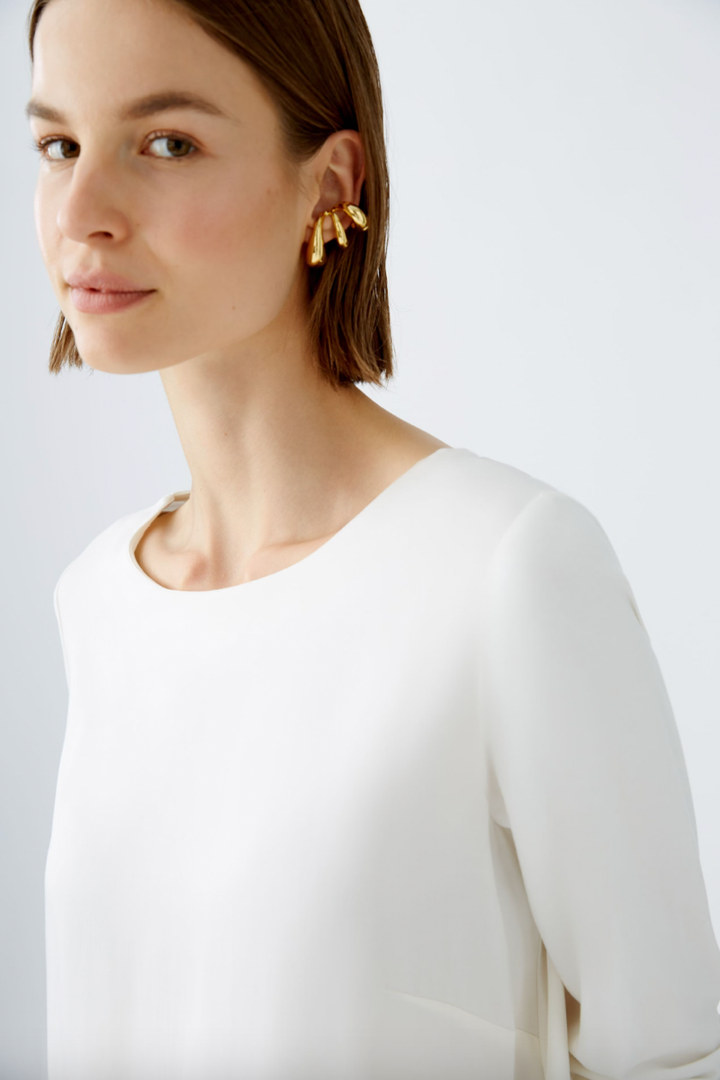 Femme portant une blouse blanche décontractée et des boucles d'oreilles dorées, style chic et élégant.