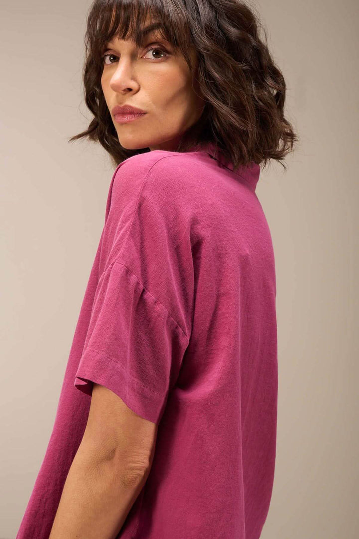 Femme portant une blouse courte en coton bio, col chemise, couleur rose, style décontracté et élégant.