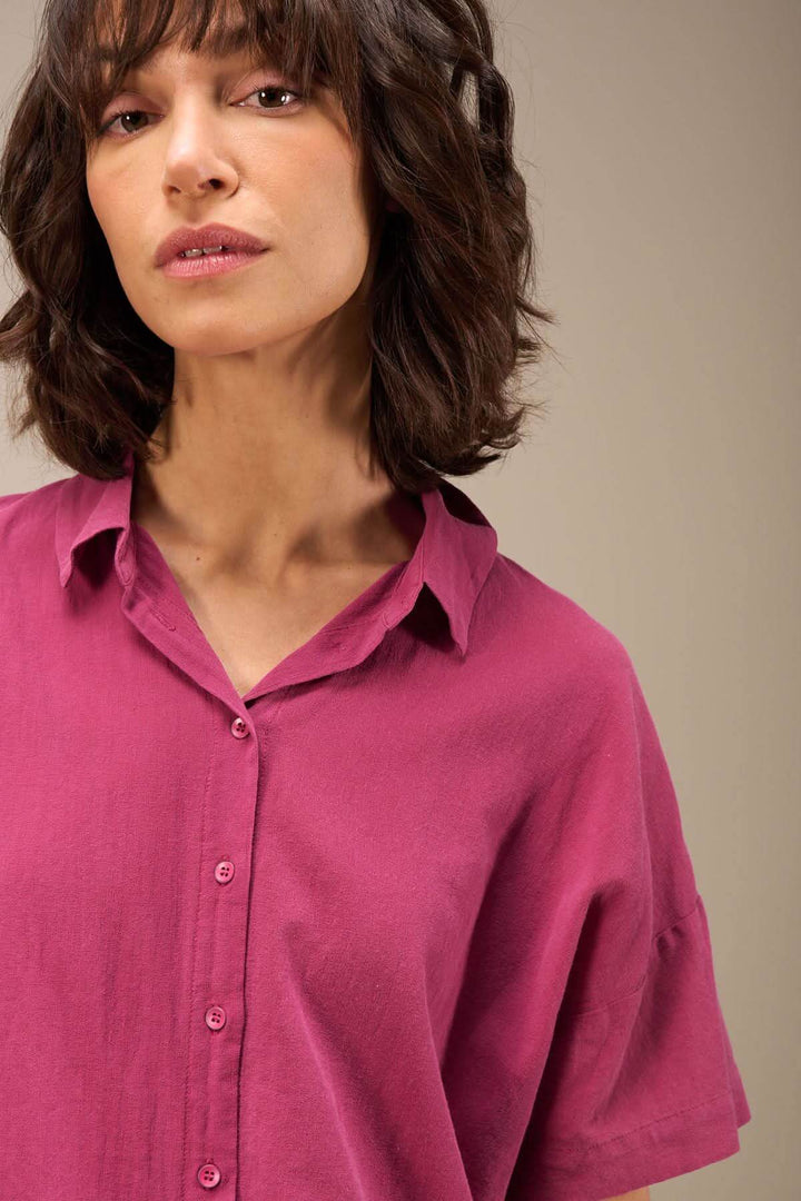 Femme portant une blouse en coton biologique rose, col chemise et manches courtes, look léger et décontracté.