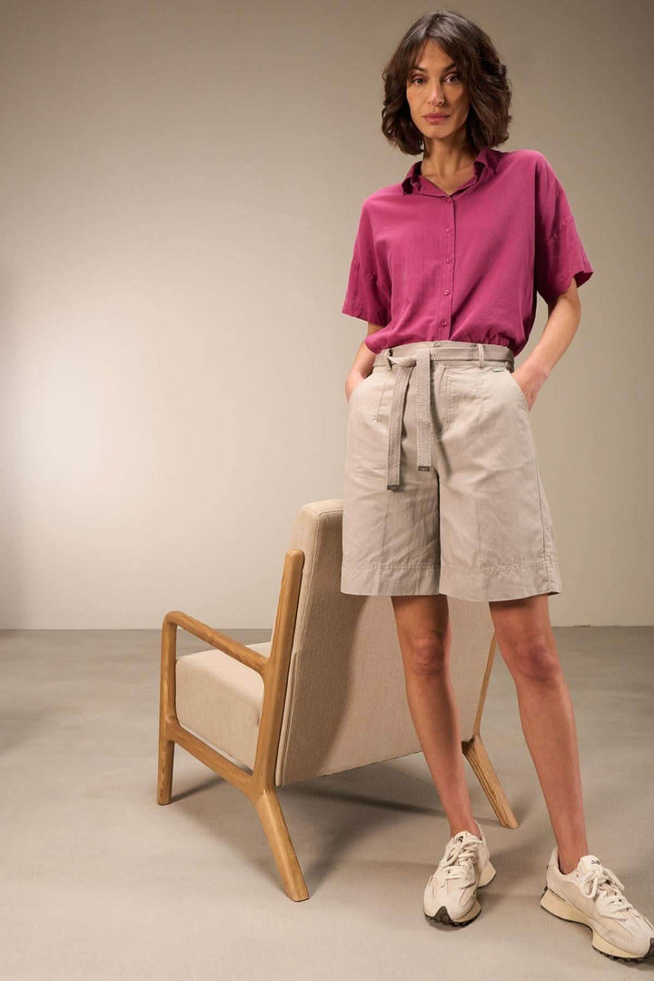 Femme portant une blouse en coton rose et un short beige, look décontracté, dans un intérieur moderne.
