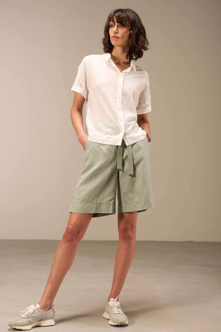 Modèle féminine portant une blouse en coton blanc et un short vert, style décontracté, look estival.
