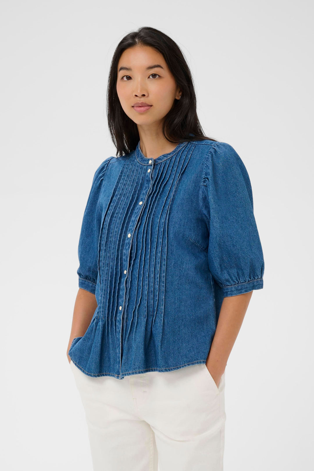 Blouse en denim Alesia avec plis décoratifs et coupe évasée, portée par une femme pour un look moderne et élégant.