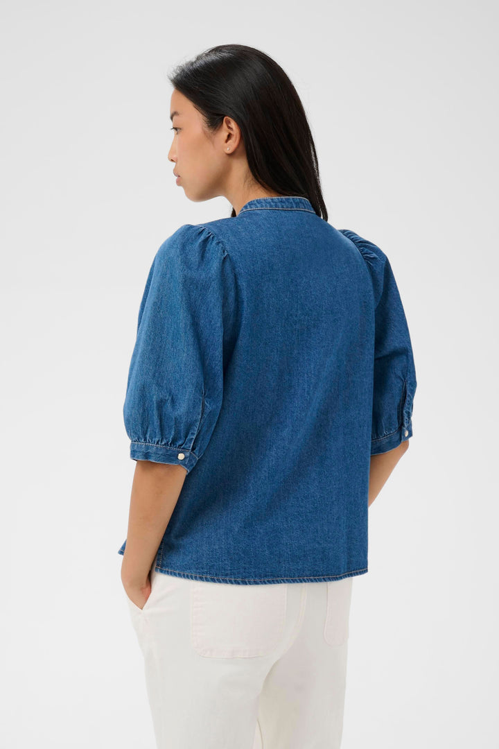 Vue arrière de la Blouse en denim Alesia avec plis décoratifs, manches bouffantes, et coupe évasée, parfaite pour une tenue moderne.