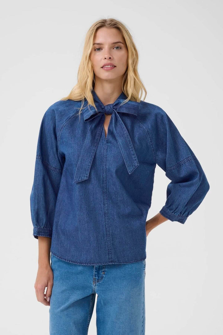 Blouse en denim léger avec col noué, manches bouffantes et coupe fluide pour un look moderne.