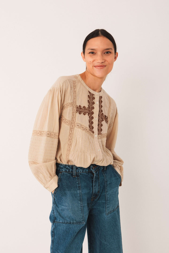 Femme portant une blouse ethnique brodée beige avec détails plissés et manches longues, associée à un jean.