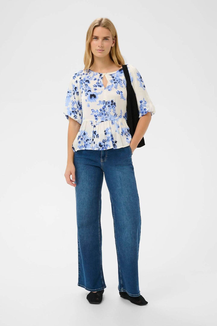 Blouse fleurie Azelia fluide à imprimé floral, coupe évasée, portée avec un sac noir. Haut féminin et facile à intégrer à toute tenue.