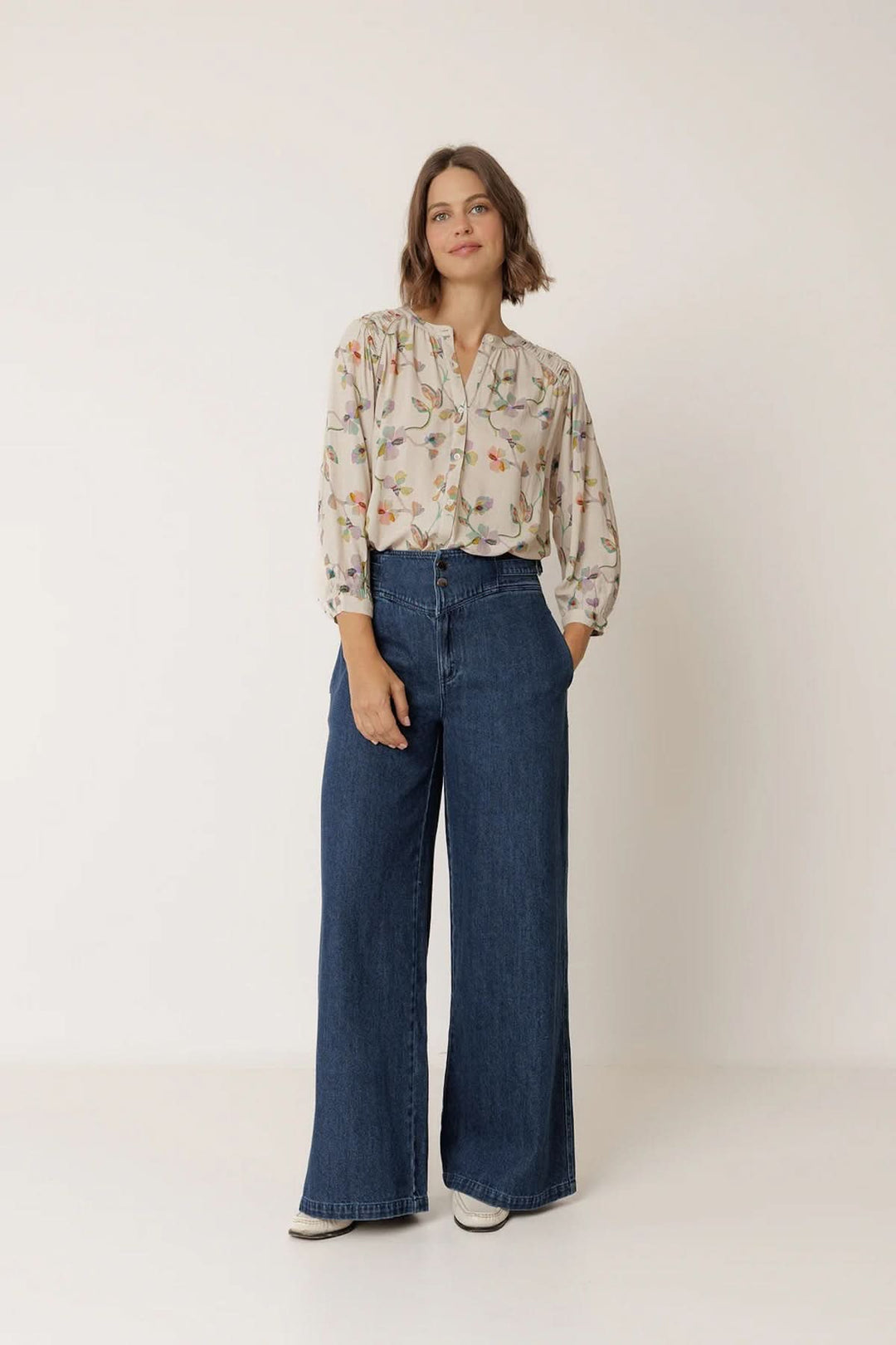Femme portant une blouse florale à manches longues avec imprimé subtil et silhouette fluide, associée à un jean, style élégant.