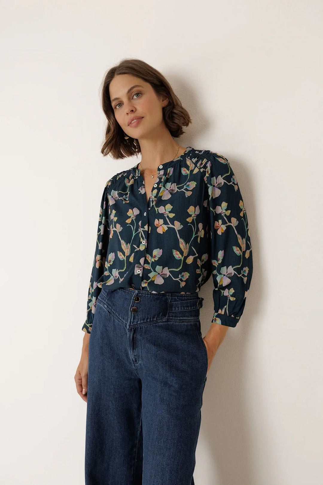Blouse florale à manches longues avec imprimé délicat et silhouette élégante, portée par une femme, fond blanc.