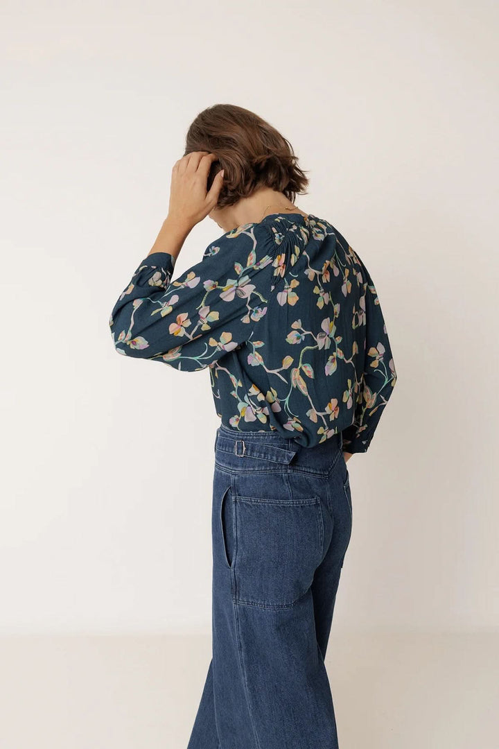 Femme portant une blouse florale à manches longues avec un motif délicat, associée à un jean pour un look élégant et confortable.