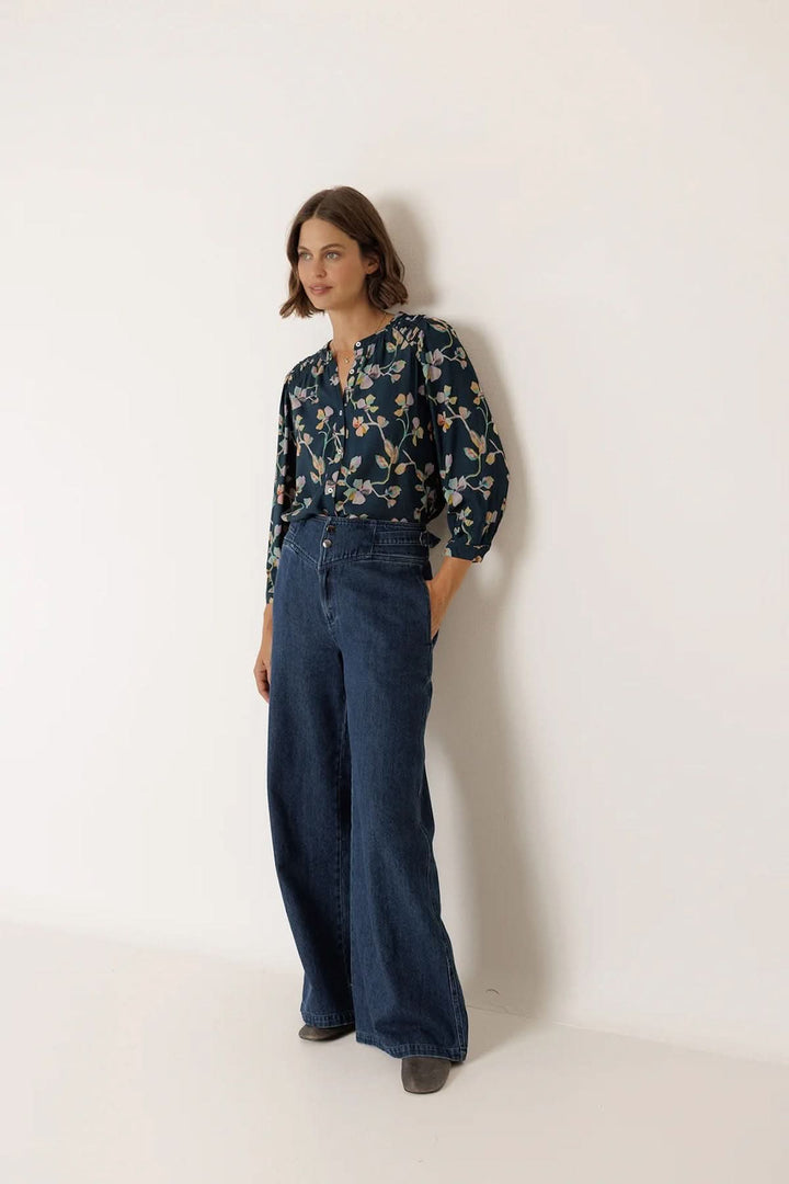 Femme portant une blouse florale à manches longues avec jeans, élégance et confort quotidiens.