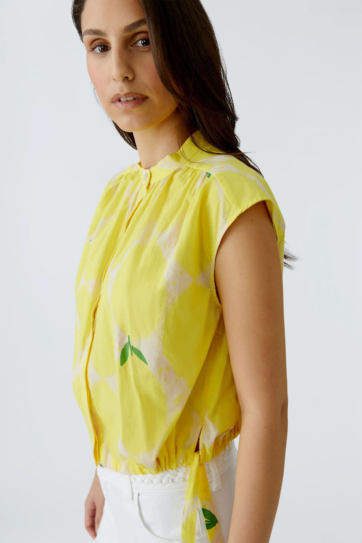 Femme portant une blouse fluide à col montant jaune sans manches, style élégant et décontracté.