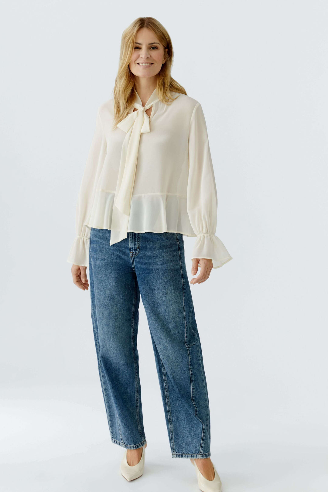 Femme portant une blouse fluide à cravate col noué avec manches longues et poignets volantés, parfait pour un look chic et féminin.