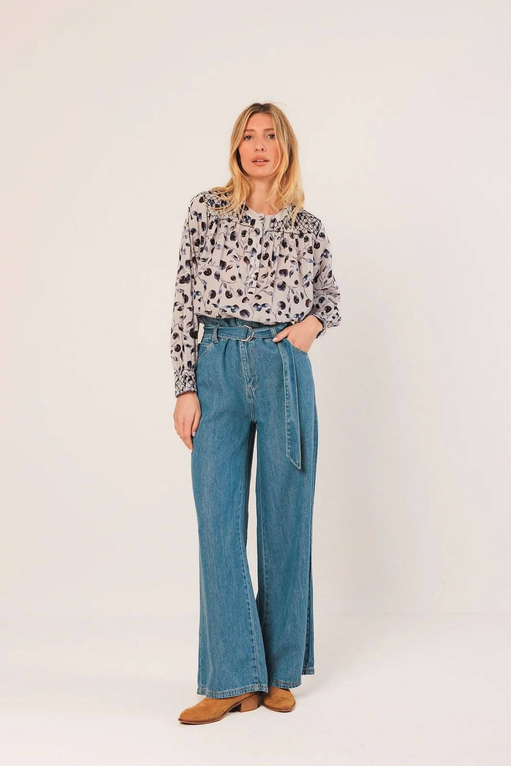 Femme portant une blouse fluide à imprimé nature avec détails smockés, associée à un jean taille haute pour un look chic et décontracté.