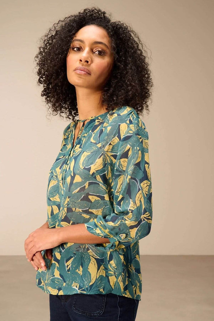 Blouse fluide imprimé avec manches 3/4 et encolure fendue, motif végétal audacieux, portée par mannequin. Style décontracté et moderne.