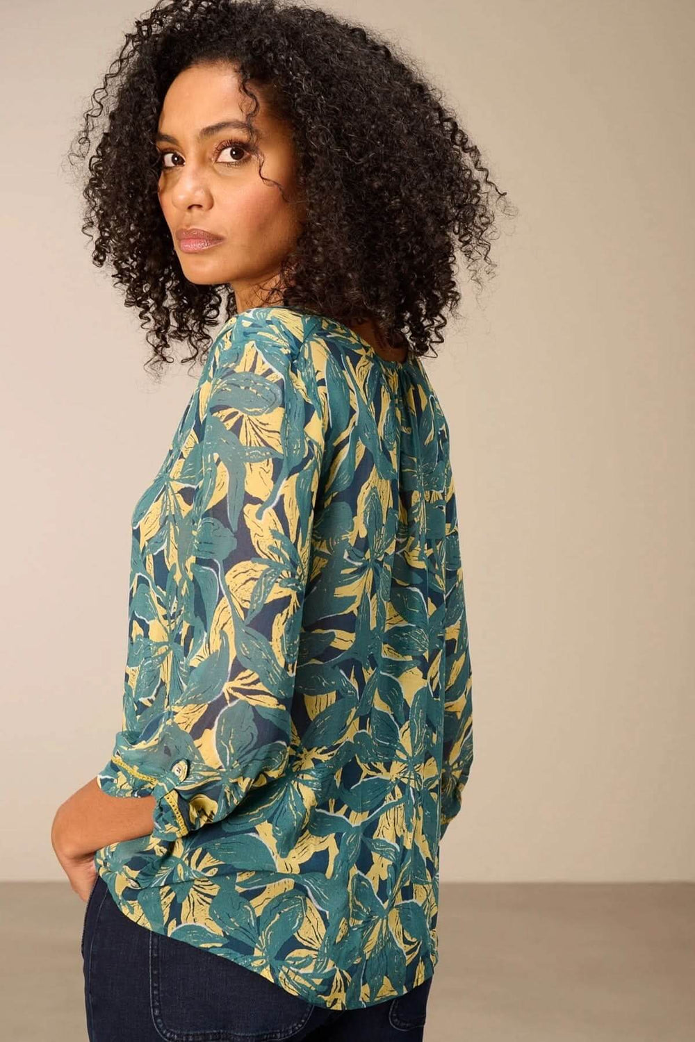 Blouse fluide imprimé avec motifs végétaux audacieux, manches 3/4 et encolure fendue, portée par une femme de profil.