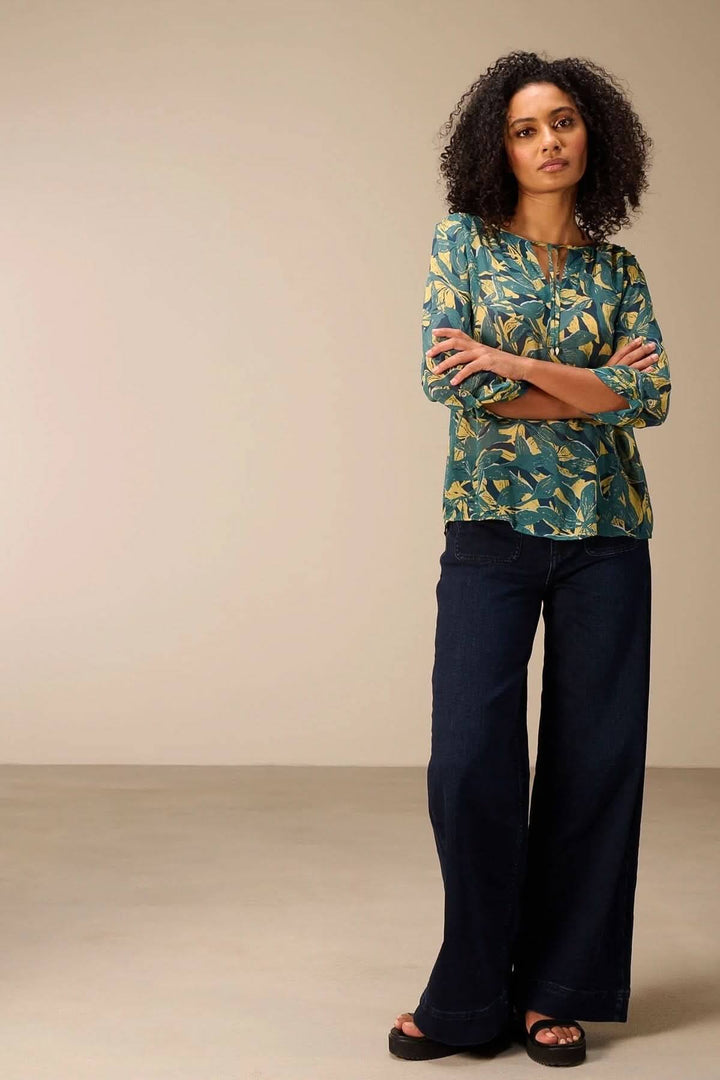 Blouse fluide imprimé à manches 3/4 et encolure fendue, portée avec un jean, ajoutant une touche féminine et moderne.