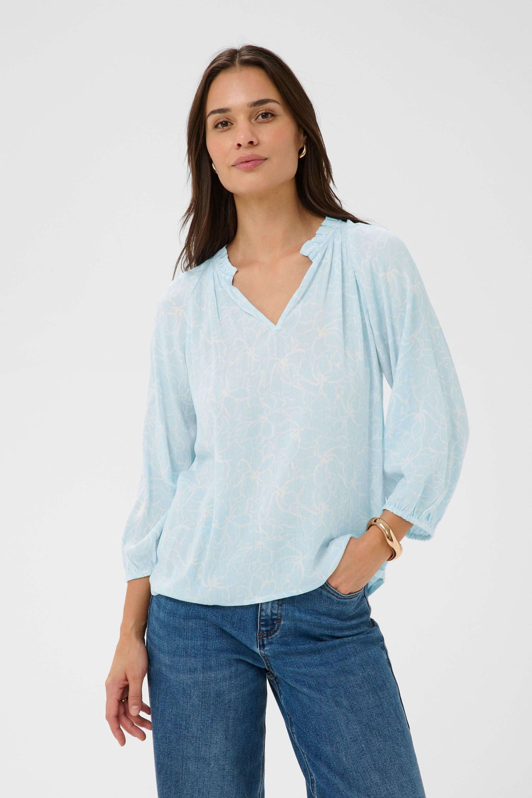 Femme portant une blouse fluide à imprimé floral discret avec encolure en V et manches trois-quarts, style léger et élégant.