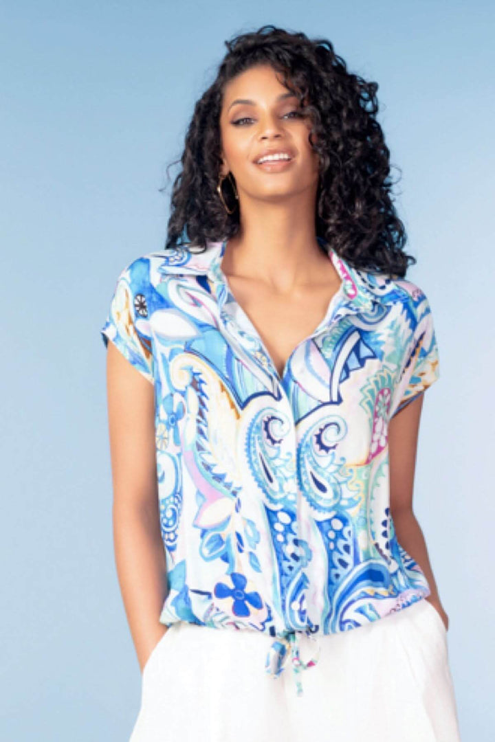 Femme portant une blouse fluide imprimée avec un motif graphique et coloré, encolure ouverte, style décontracté et chic.