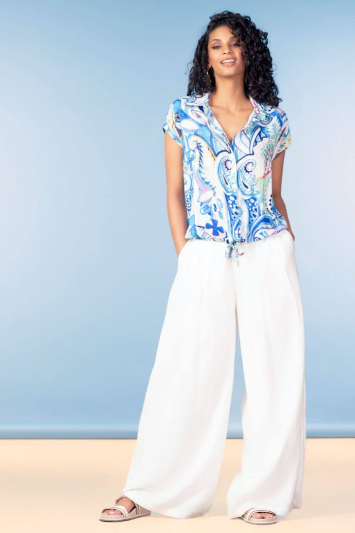 Blouse fluide imprimée avec imprimé graphique et encolure ouverte, portée avec un pantalon large blanc. Décontractée et féminine.