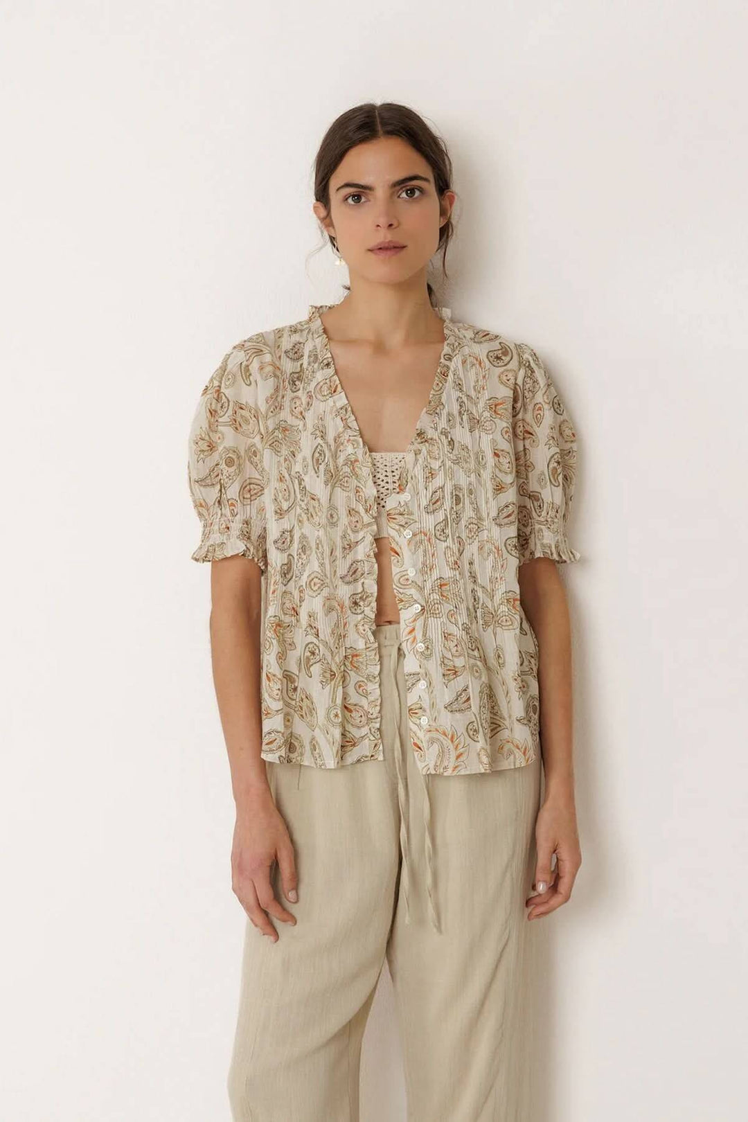 Blouse fluide imprimée à manches courtes avec encolure en V et finition volantée, portée par un modèle féminin devant un fond uni.