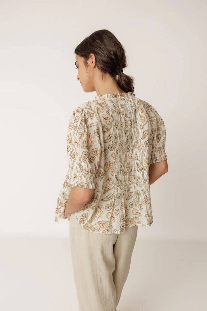 Femme portant une blouse fluide imprimée à manches courtes, vue dos, avec imprimé délicat et manches légèrement bouffantes, encolure travaillée.