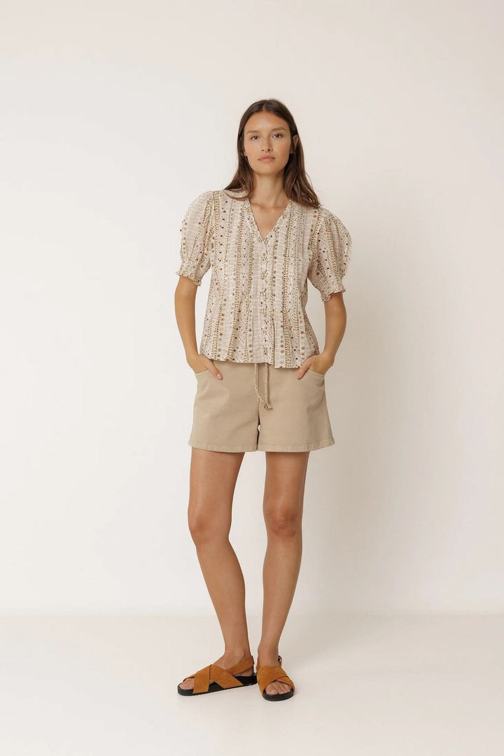 Blouse fluide imprimée à manches courtes avec encolure en V et manches bouffantes, portée avec un short beige et sandales.
