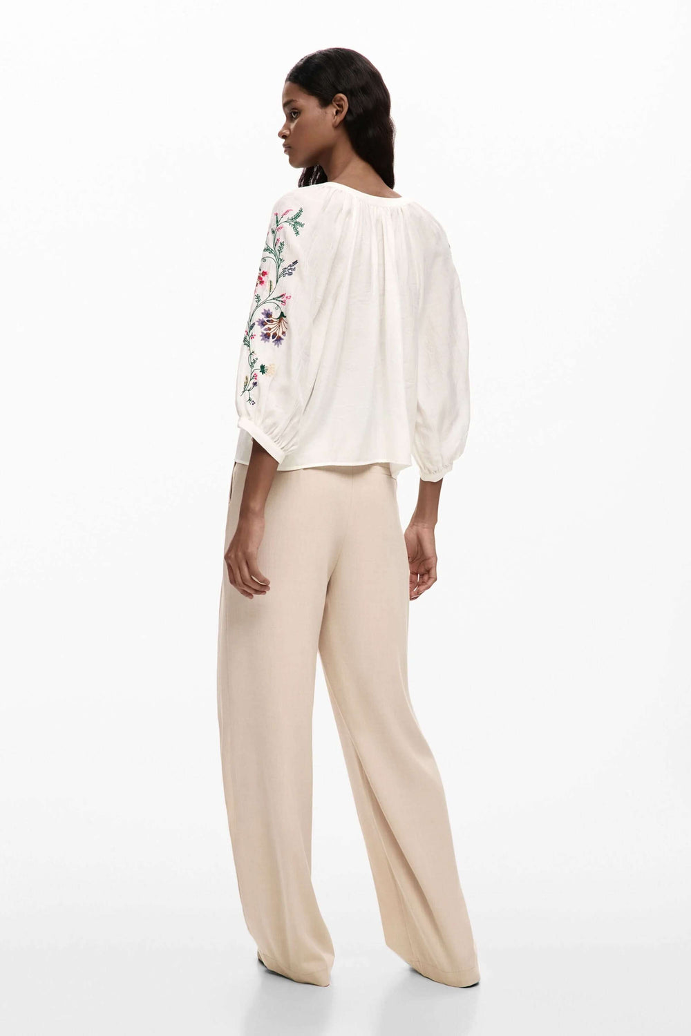 Blouse fluide à manches brodées portée avec un pantalon beige, montrant des détails brodés et une coupe ample et élégante.
