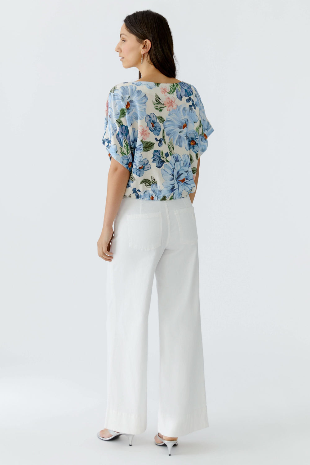 Vue arrière d'une blouse fluide à manches courtes, silhouette légère et féminine, portée avec un pantalon blanc élégant.