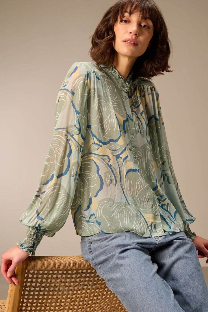 Blouse fluide à manches longues élégante au motif floral, portée avec un jean, pour une tenue féminine et confortable.
