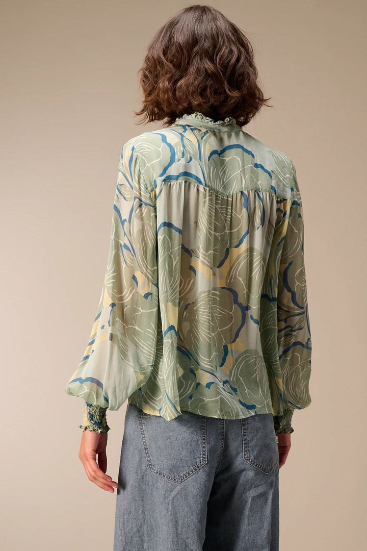 Femme portant une blouse fluide à manches longues, col montant, tissu à motifs et poignets smockés, vue arrière.