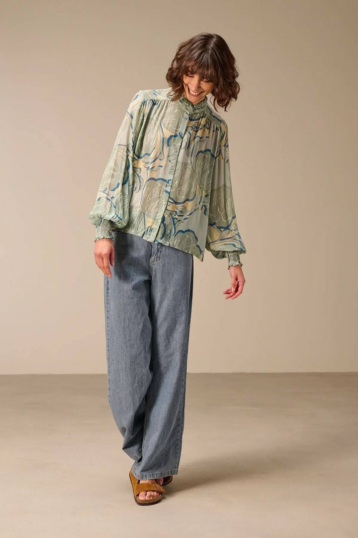 Blouse fluide à manches longues en tissu fluide avec motif, portée avec un col montant et manches volumineuses, idéale pour mi-saison.
